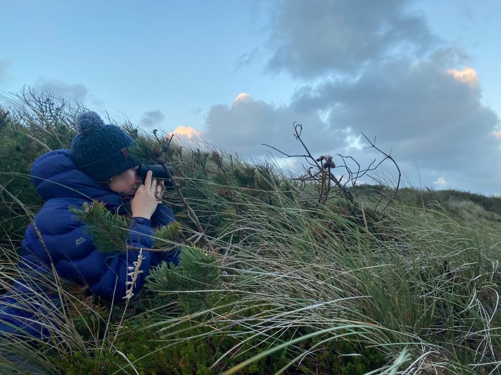 Elena Pearce using a binoculars in tall grass